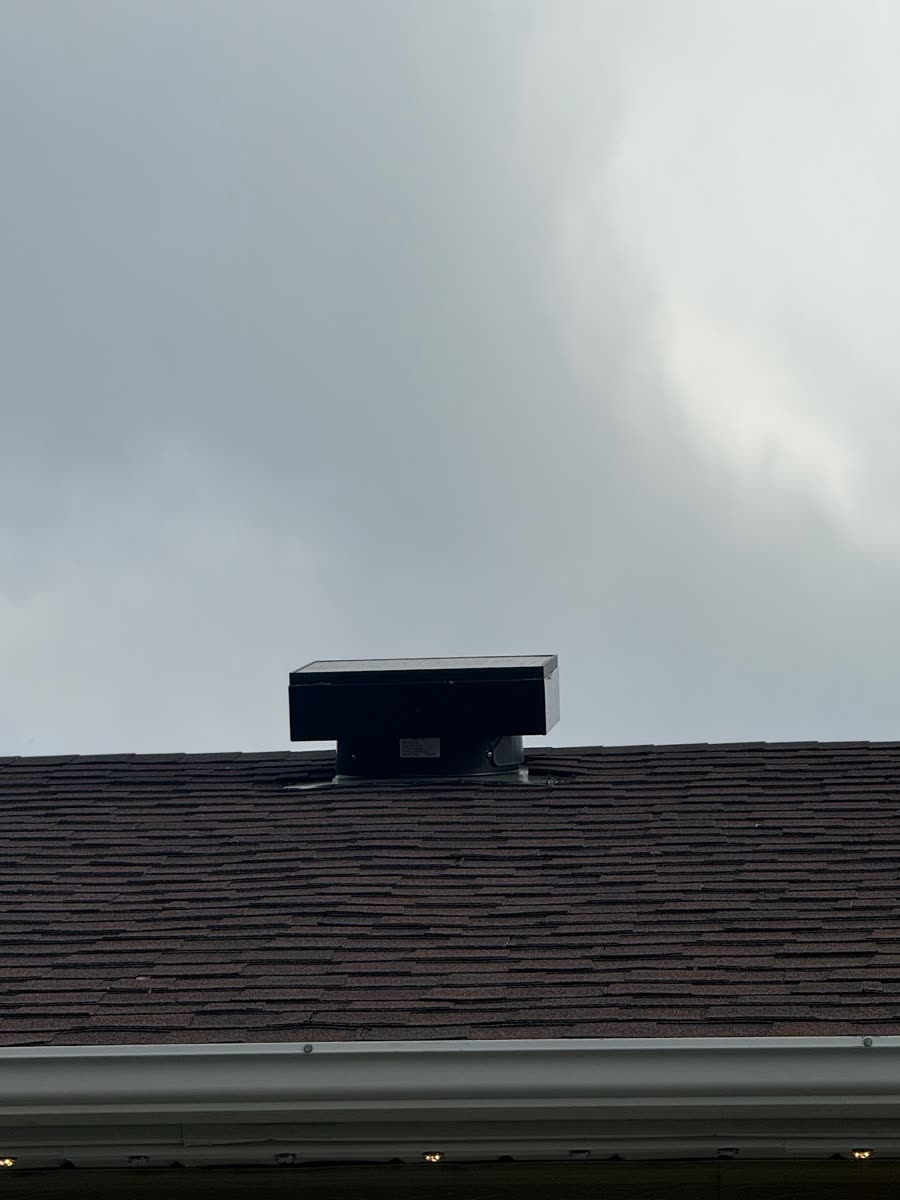 Solar-powered attic fan mounted near the ridge of a roof